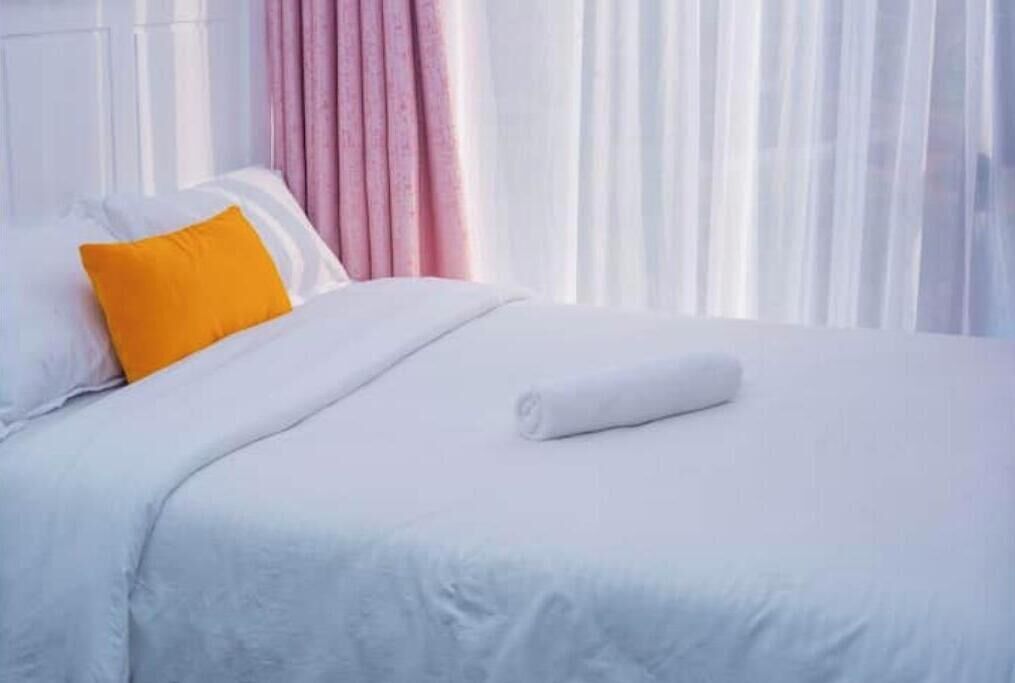 Una cama bien hecha con ropa blanca y una única almohada naranja brillante.