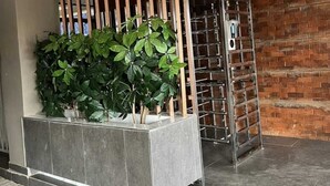 Un área de recepción con una planta, un panel divisor de listones de madera, un estante metálico y una pared de ladrillo.