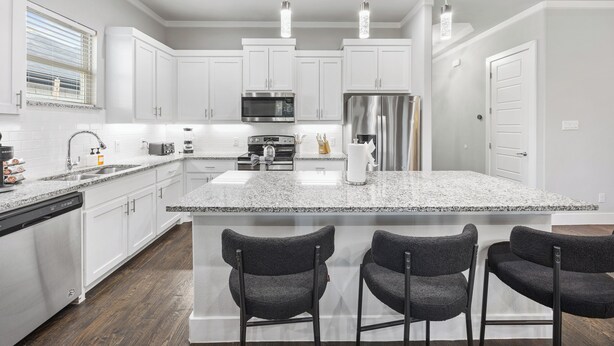 Eine moderne Küche mit weißen Schränken, Granit Arbeitsplatten, einem Edelstahl-Kühlschrank und einer zentralen Kochinsel mit Barhocker.