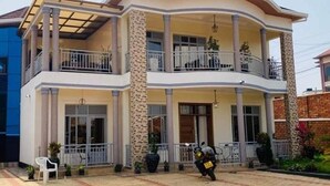 A two-story house with a balcony on the upper floor, a covered porch, and a paved driveway. - kigali fine stay (Kigali)