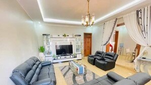 A modern living room with two black sofas, a TV, and a dining area with a table and chairs. - kigali fine stay (Kigali)
