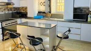 A modern kitchen with a central island, bar stools, a stove, and a microwave. - kigali fine stay (Kigali)