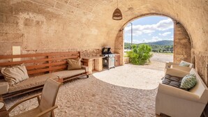 Una habitación con paredes de piedra, un banco de madera, una mesa pequeña y una parrilla.