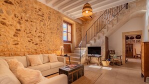 Amplia sala de estar con pared de piedra, una escalera, un sofá, un televisor y un aparador de madera rústica.