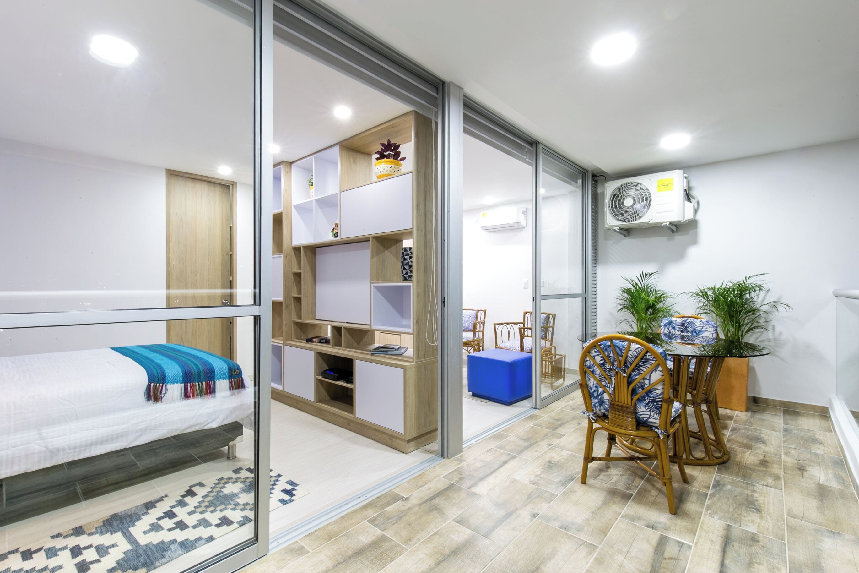 Een moderne kamer met een bed, een bureau, een stoel, een klein tafeltje en een plant in een pot.