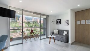A modern living room with a large window, a grey sofa, a small round table, and a blue chair. - Borbon Suites (Medellin)