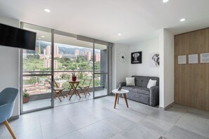 A modern living room with a large window, a grey sofa, a small round table, and a blue chair. - Borbon Suites (Medellin)