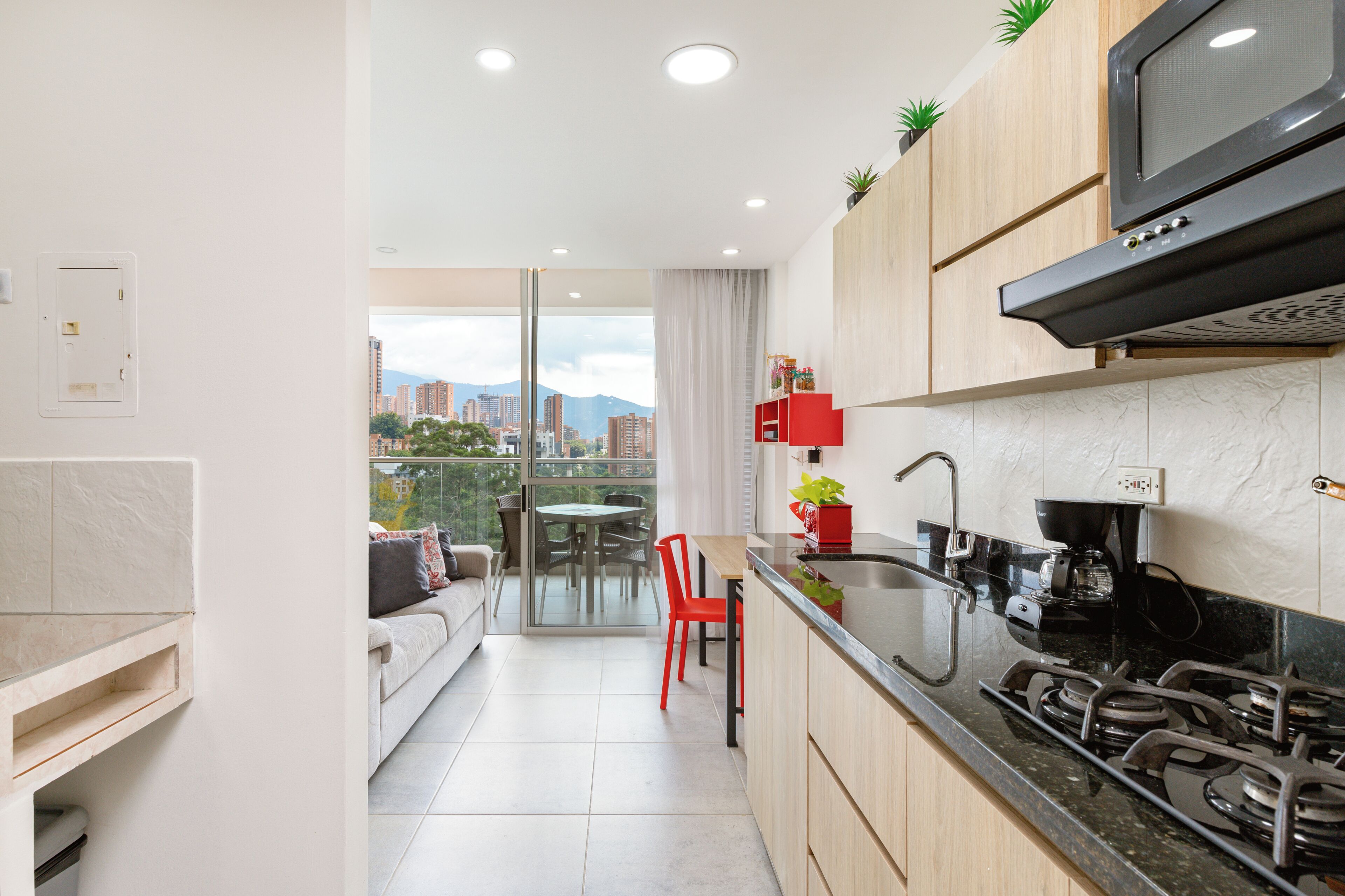 Una cocina moderna con estufa a gas, microondas y vistas a la ciudad a través de un ventanal.