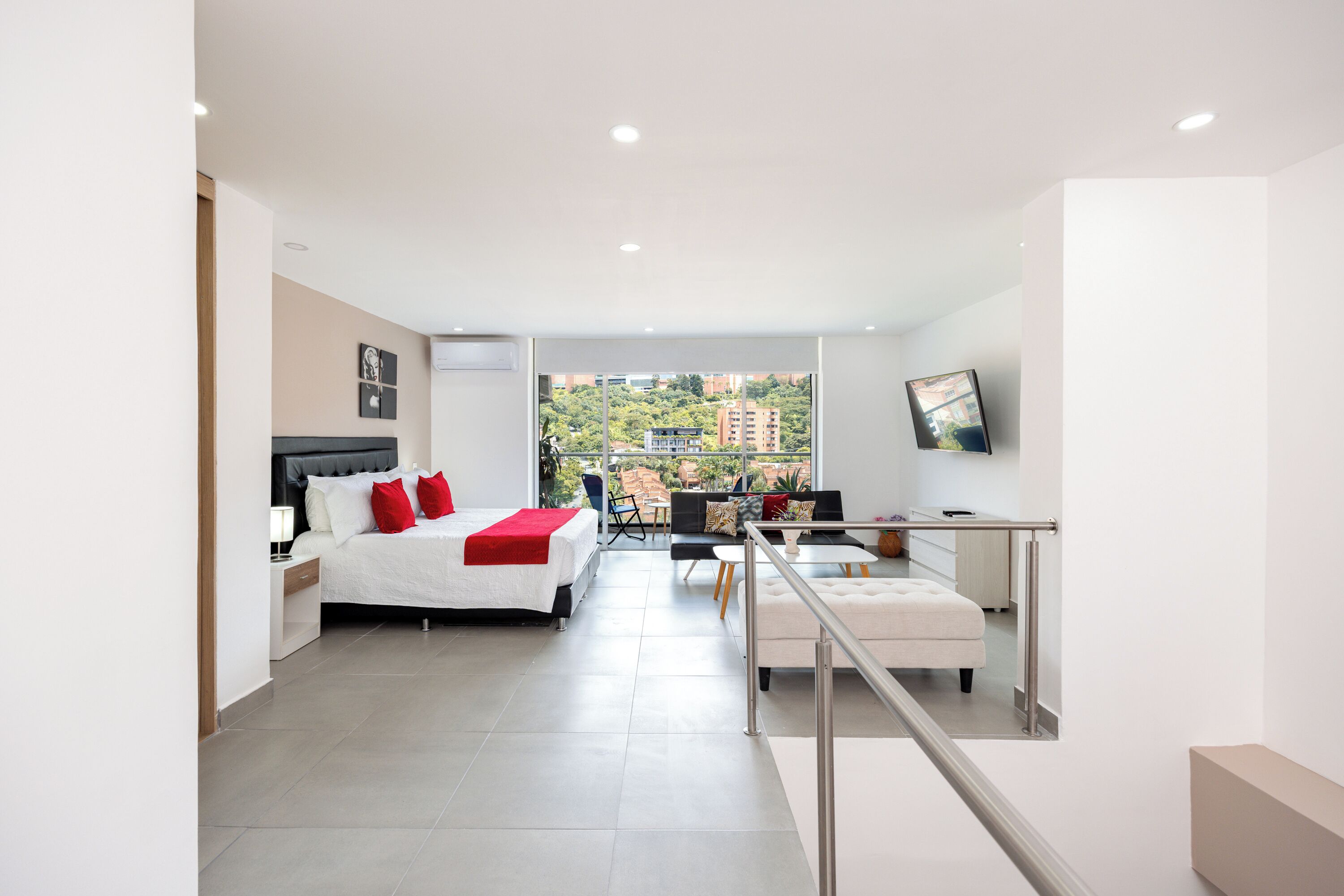 A modern hotel room with a bed, a desk, and a balcony with a city view.