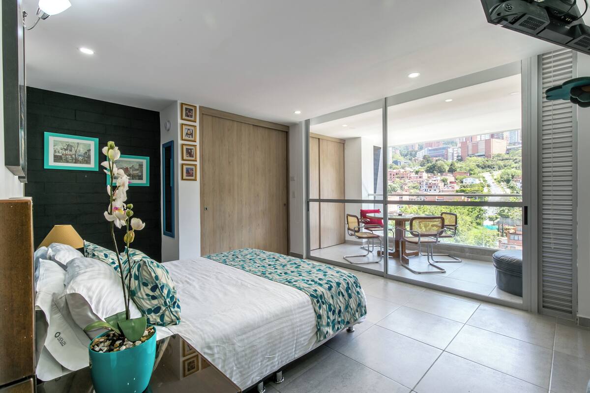 A modern bedroom with a bed, a potted orchid, and a balcony with a view of the city.