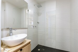 A modern bathroom with a large white vessel sink, a mirror, a shower with a handheld showerhead, and a black tiled floor. - Borbon Suites (Medellin)