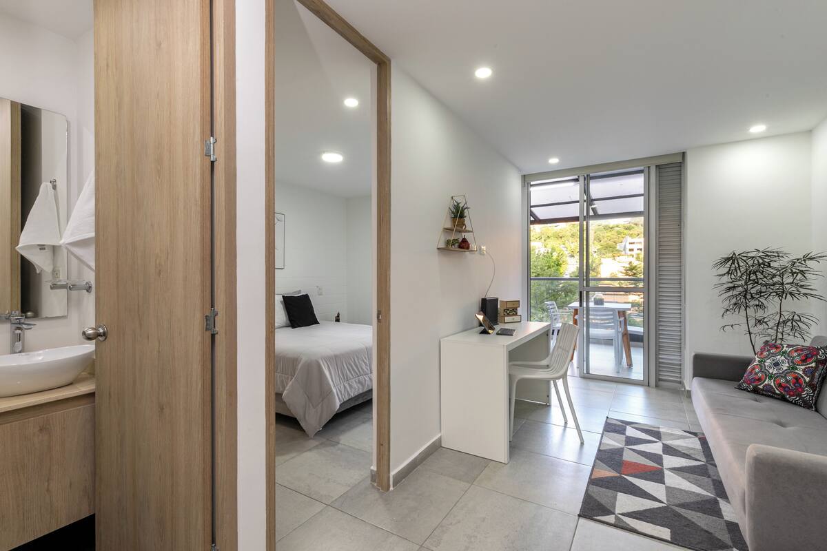A modern bedroom with a bed, a desk, and a view of the outdoors.