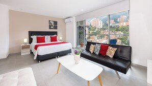 A modern hotel room with a large bed, a black sofa, a white coffee table, and a city view through large windows. - Borbon Suites (Medellin)