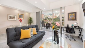 A modern living room with a black sofa, a glass coffee table, and a view of the city through large windows. - Borbon Suites (Medellin)