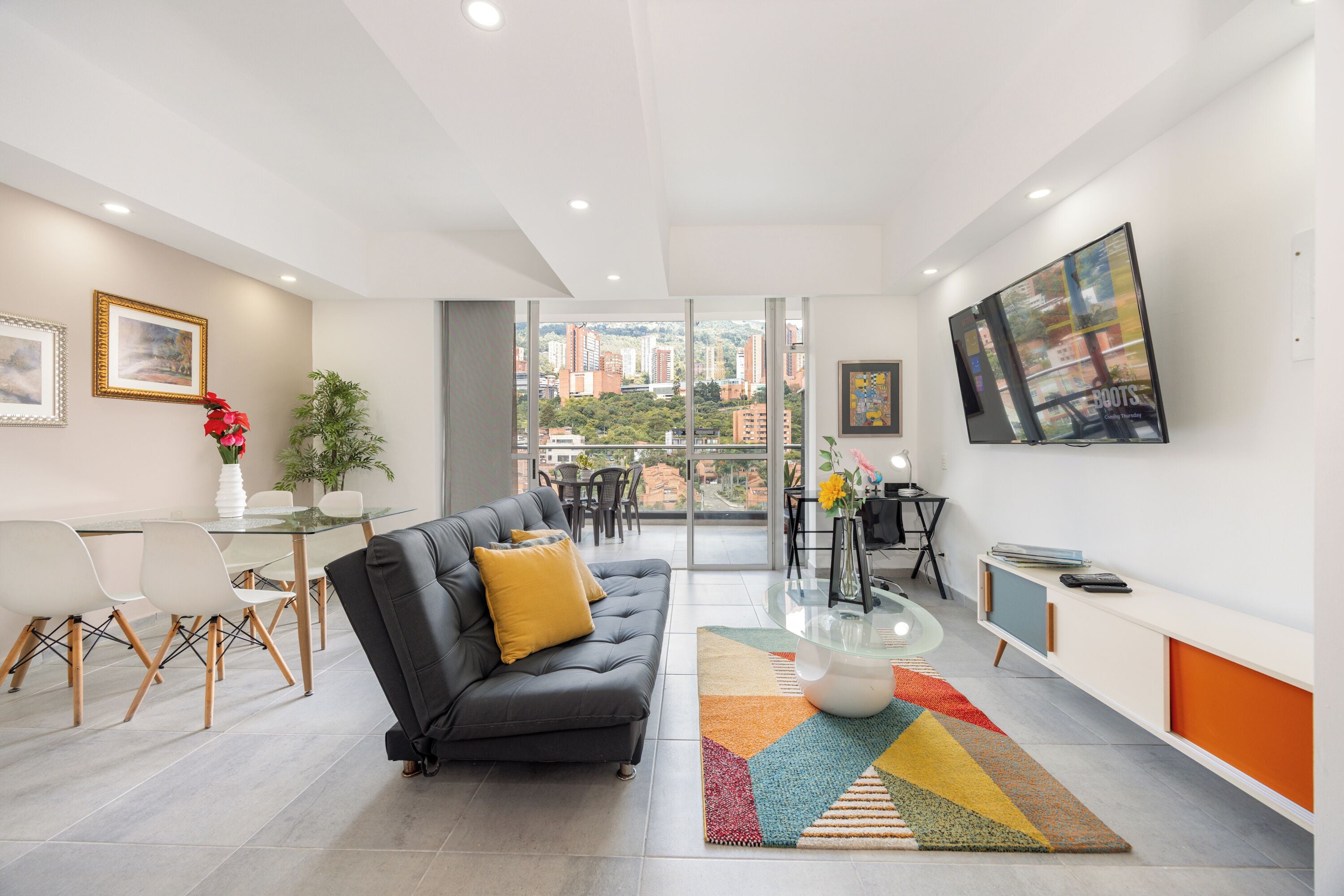 Uma sala de estar moderna com sofá, mesa de jantar, cadeiras e uma grande janela com vista para a cidade.