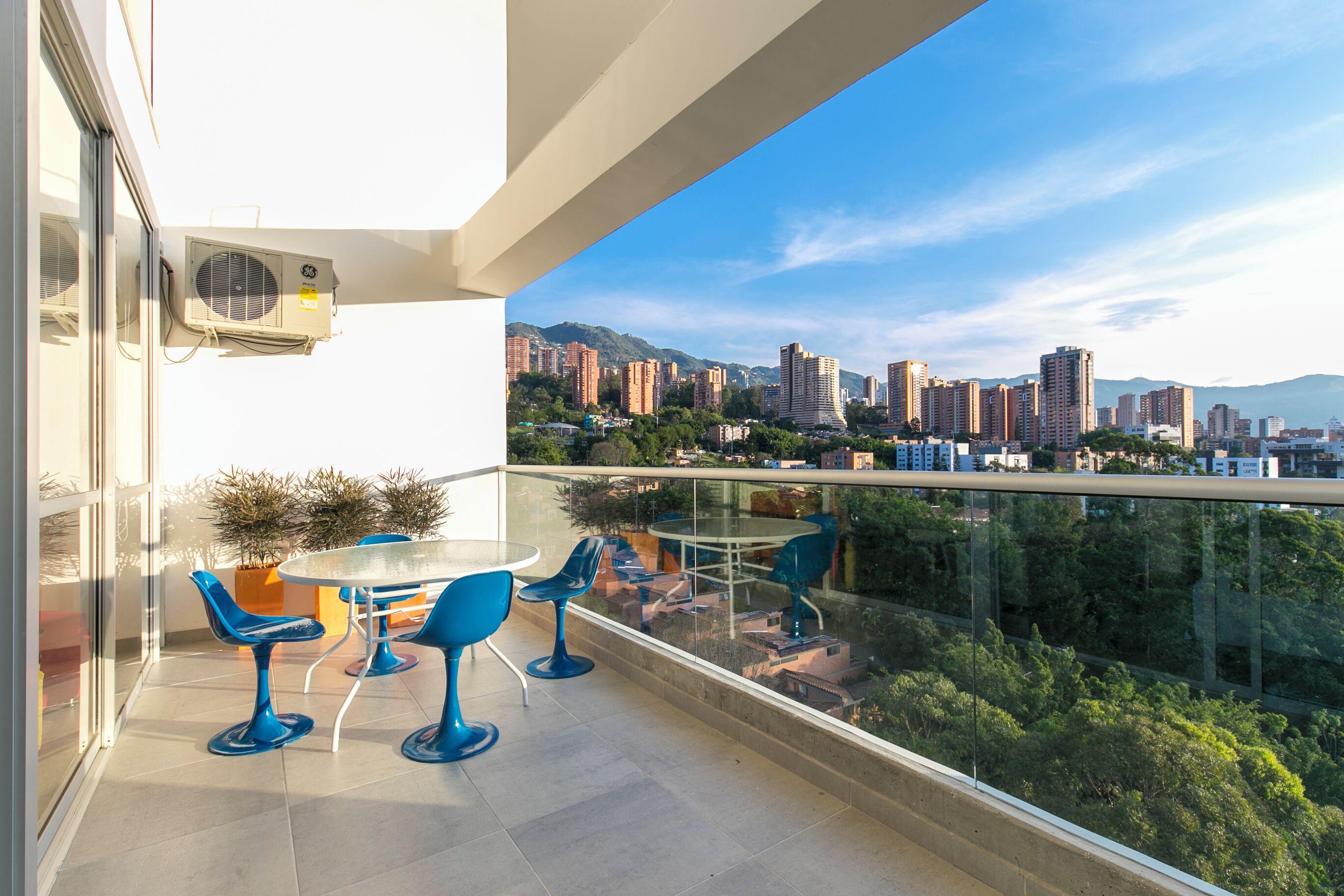 Ein Balkon mit Glasgeländer, einem Tisch und Stühlen sowie Blick auf die Stadt.