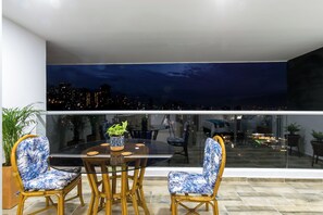 A dining area with a glass table and chairs, a potted plant, and a city view at night. - Borbon Suites (Medellin)