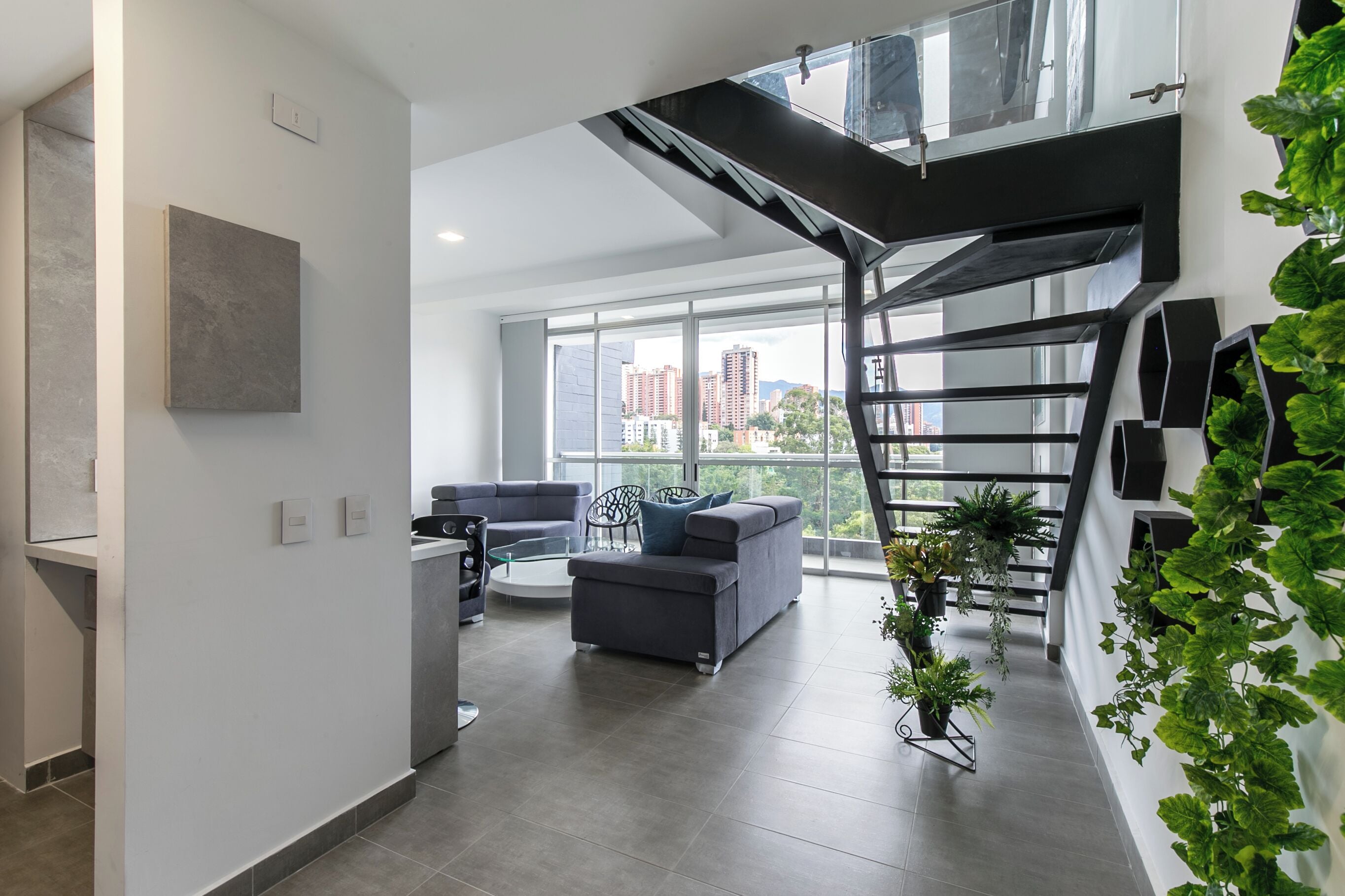 A modern living room with a gray sofa, a coffee table, and a staircase with a glass railing.