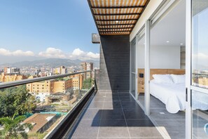 A balcony with a city view, a bed, and a glass door leading to a room. - Borbon Suites (Medellin)