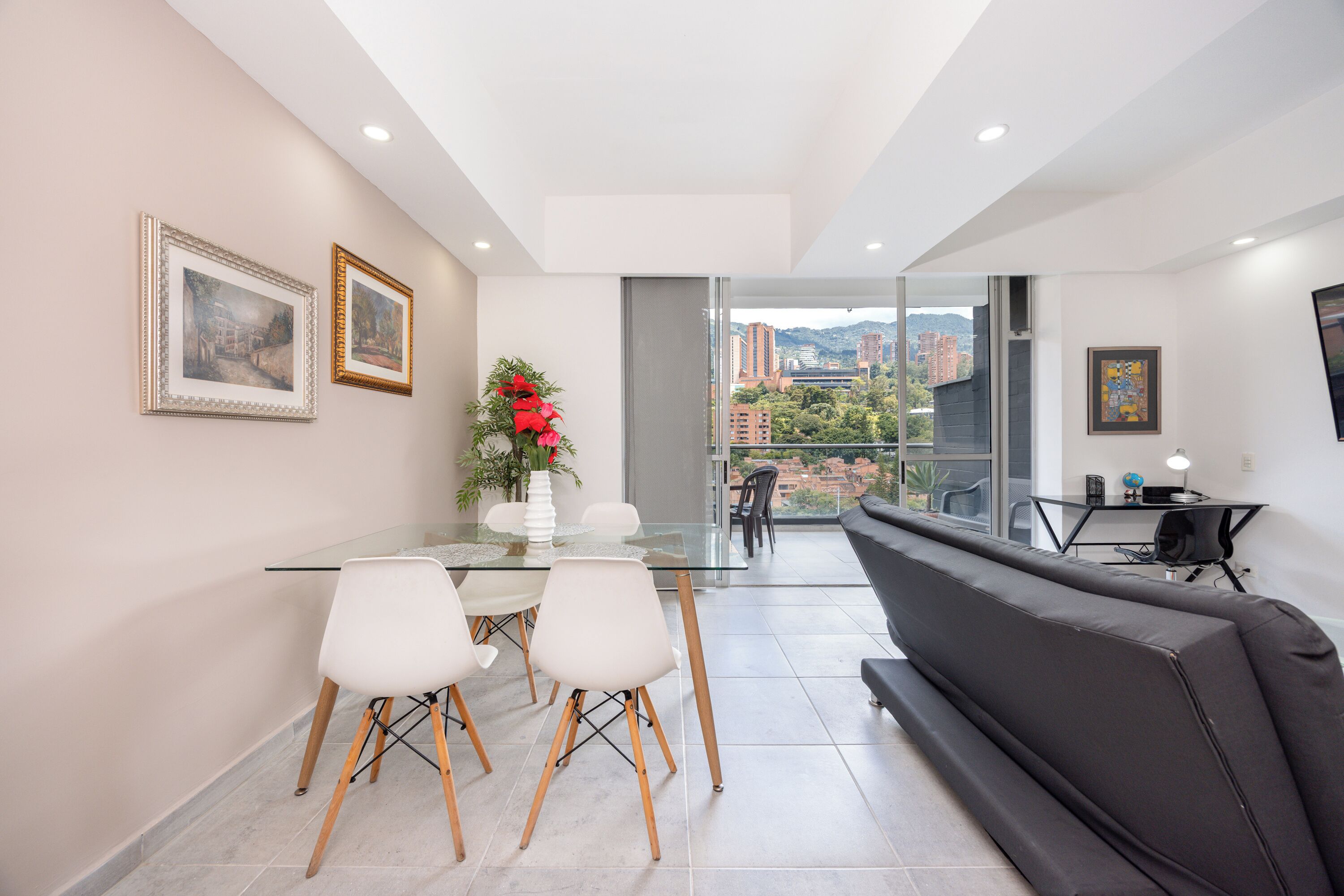 Un salon moderne avec une table à manger en verre, des chaises blanches, un canapé noir et un balcon offrant une vue sur la ville.