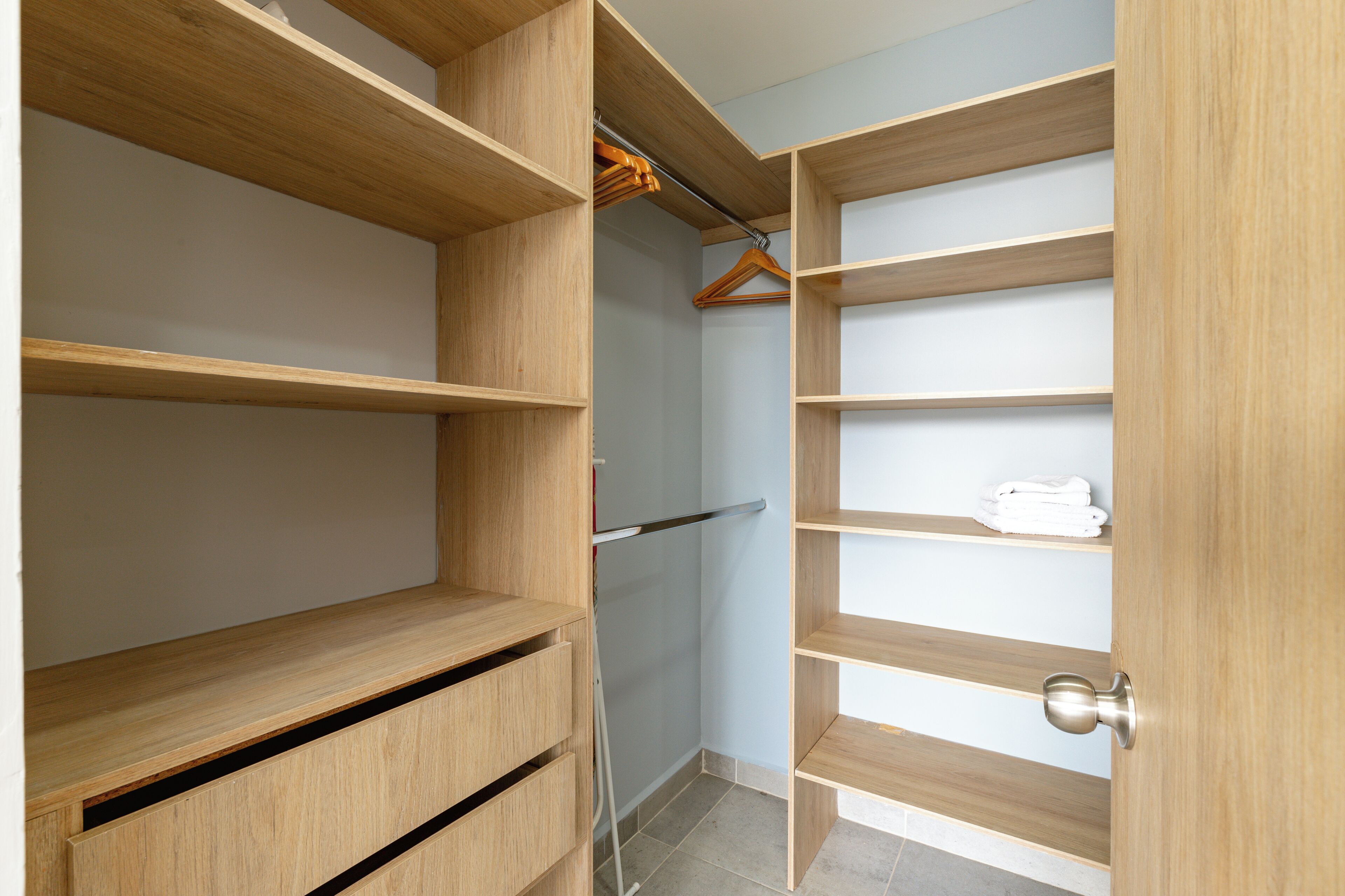 A walk-in closet with open shelves, a hanging rod, and a door with a silver handle.