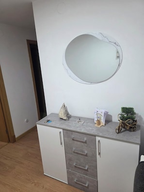 A room with a white cabinet, a round mirror, a small statue, a plant, and a door. - SNEY'S HOUSE (Sarria)