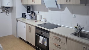 Uma cozinha moderna com armários de madeira clara, forno embutido, micro-ondas e aquecedor de água.