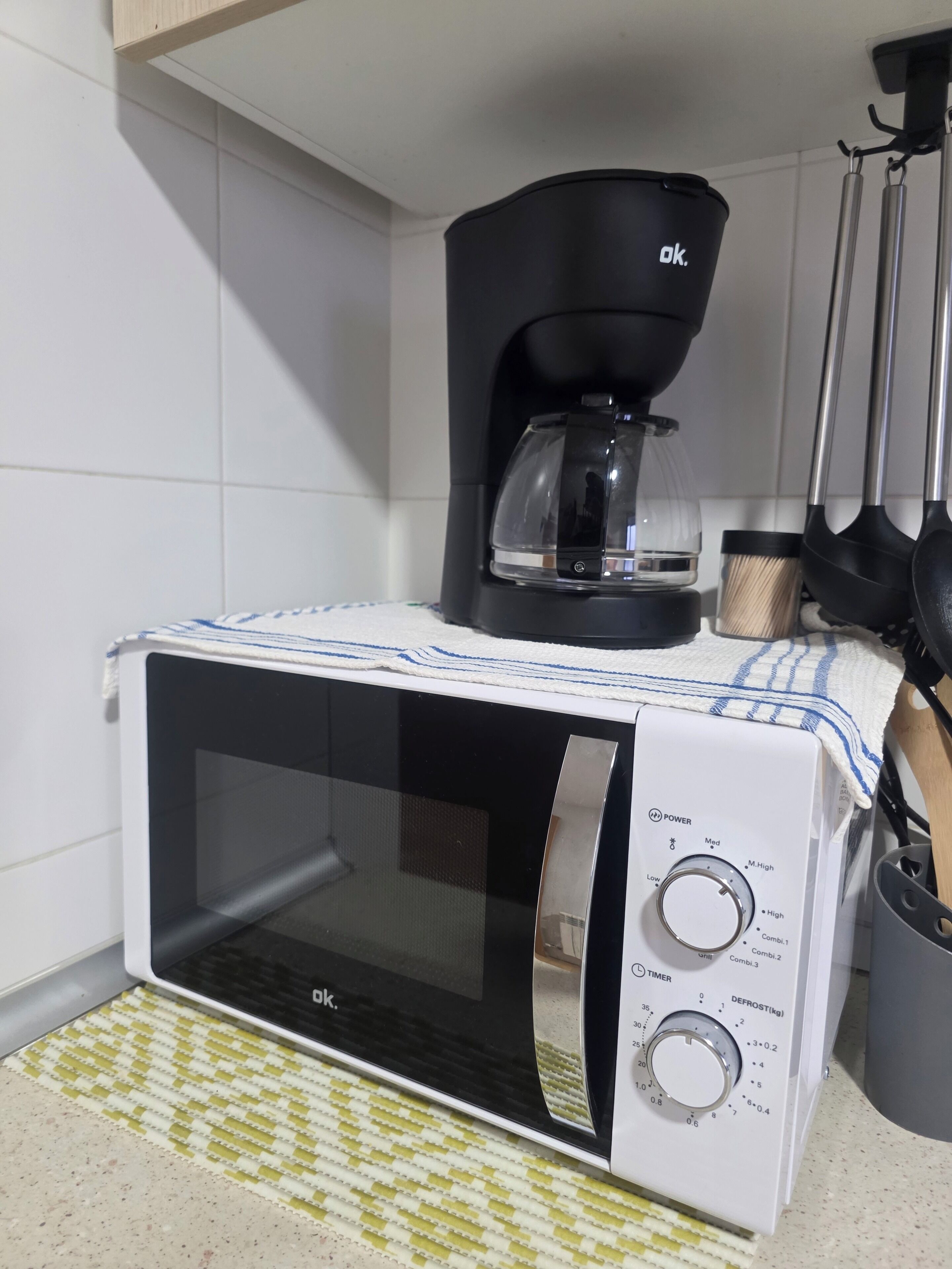 Un microondas con temporizador y ajustes de potencia, una cafetera y un organizador de utensilios de cocina.