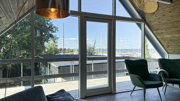 Ein modernes Interieur mit großen Fenstern, Blick auf eine Marina und einer Holzbalkendecke.