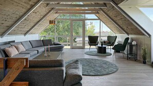 Ein geräumiger Loft mit geneigter Decke, einer großen Couch, einem Couchtisch und einer Sitzecke mit Stühlen.