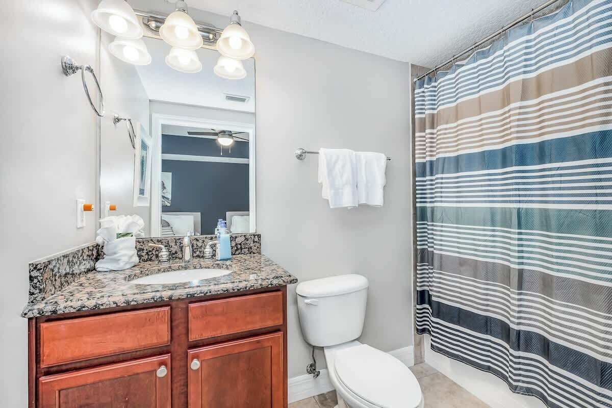 A bathroom with a granite countertop sink, wooden cabinets, a white toilet, and a striped shower curtain.