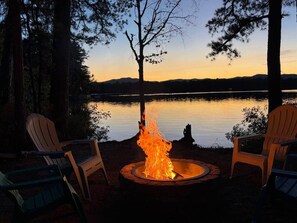Lejrild med to Adirondack-stole, der vender ud mod en rolig sø i solnedgangen.