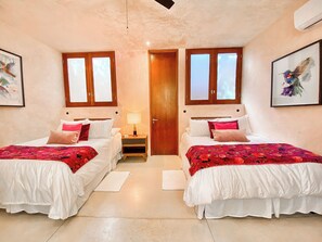 A double room with two beds, a nightstand, a lamp, and a door.