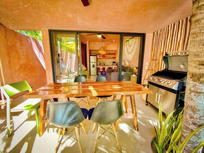 An outdoor dining area with a wooden table and chairs, a grill, and a view of the backyard.