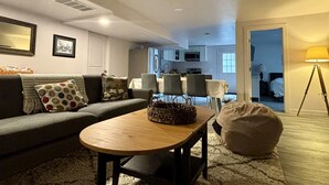 A living room with a sofa, a coffee table, and a bean bag. There is a dining area with chairs and a table in the background.