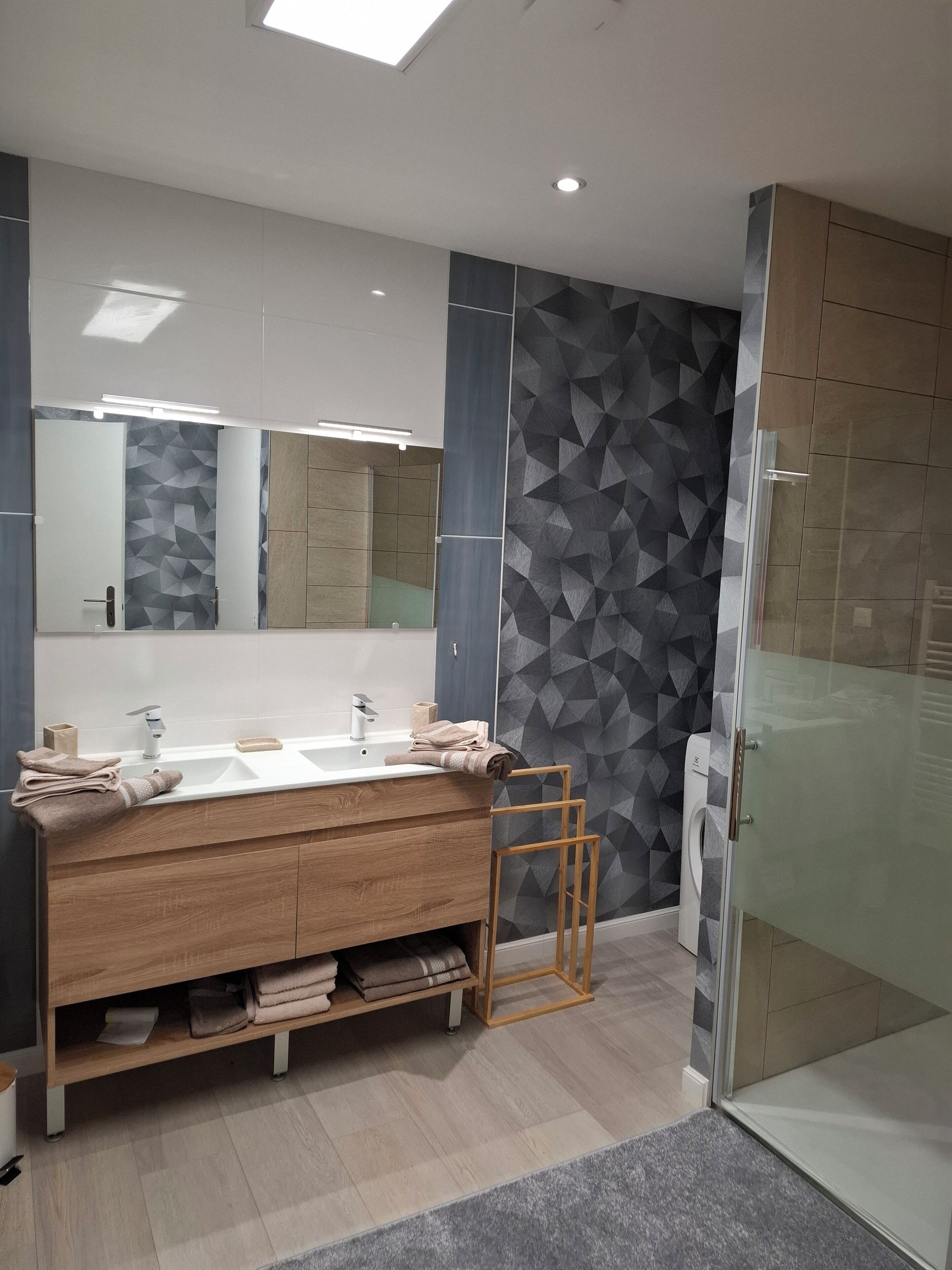 A modern bathroom with a large mirror, dual sinks, and a glass shower enclosure.