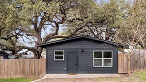 Une petite maison en bois de couleur sombre, avec un toit à pignon, deux fenêtres et une porte.