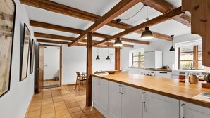 Cocina con vigas de madera, armarios blancos y encimera de madera.