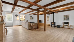 Un amplio salón con vigas de madera a la vista, un sofá, una mesa y una chimenea.