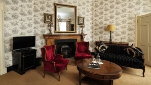 A room with a fireplace, red velvet chairs, a black sofa, a wooden coffee table, and a television. - Fitzpatrick Castle Hotel (Dublin)