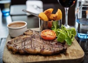 A steak with a side of fries, a small tomato, and a cup of sauce on a wooden board. - Fitzpatrick Castle Hotel (Dublin)