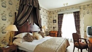 A hotel room with a large bed, a nightstand with a lamp, a chair, and a desk with a computer. - Fitzpatrick Castle Hotel (Dublin)