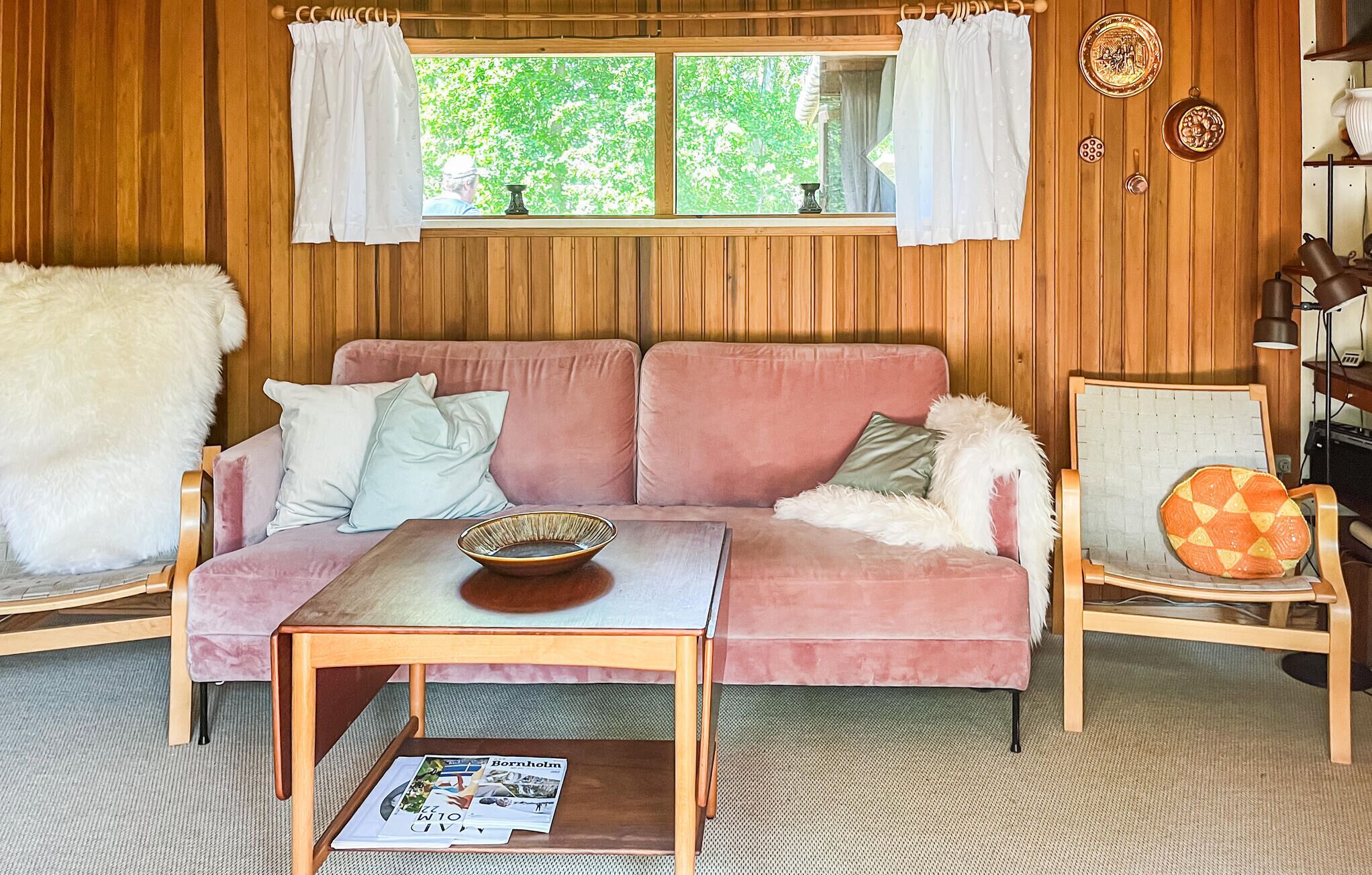 A cozy room with a pink sofa, a wooden coffee table, a white furry rug, and a window with curtains.