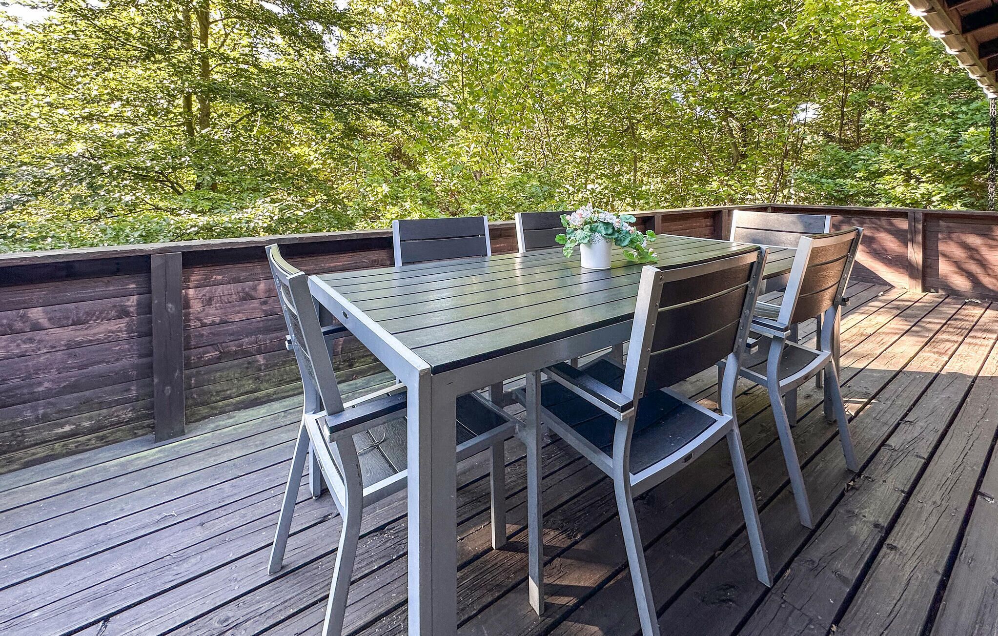 Una terraza de madera con una mesa y sillas, rodeada de árboles.
