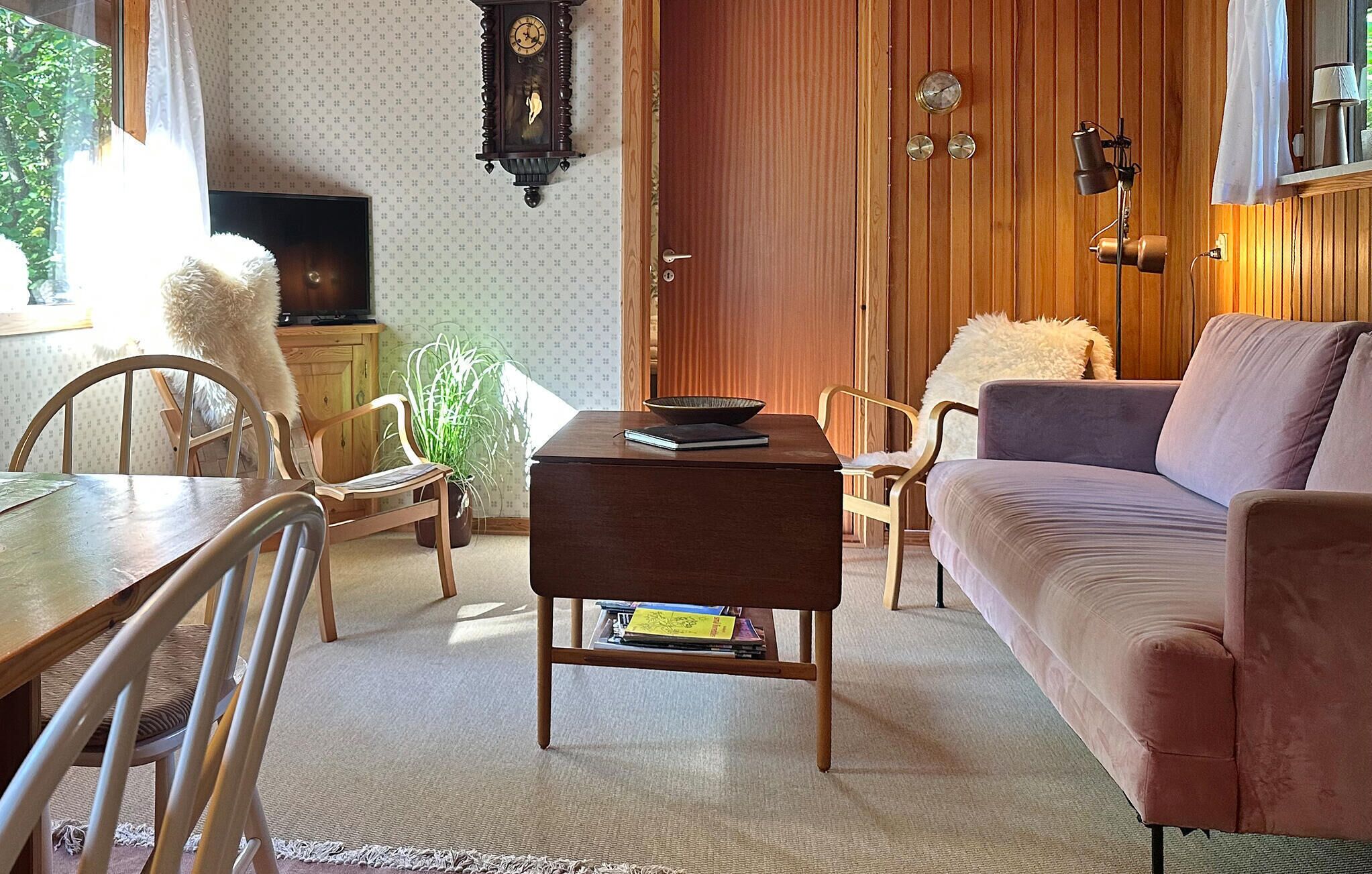 A cozy living room with a wooden coffee table, a sofa, and a dining table with chairs. There is a plant on the coffee table and a bookshelf in the corner.