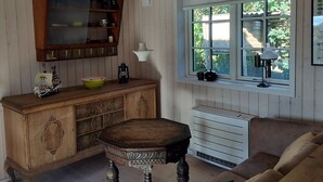 A room with a wooden ceiling, a wooden cabinet with glass doors, a window with a view of greenery, and a brown sofa. - Newly built holiday home with a fjord view (Orø)