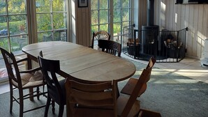 A room with a round wooden table, chairs, a fireplace, and large windows. - Newly built holiday home with a fjord view (Orø)