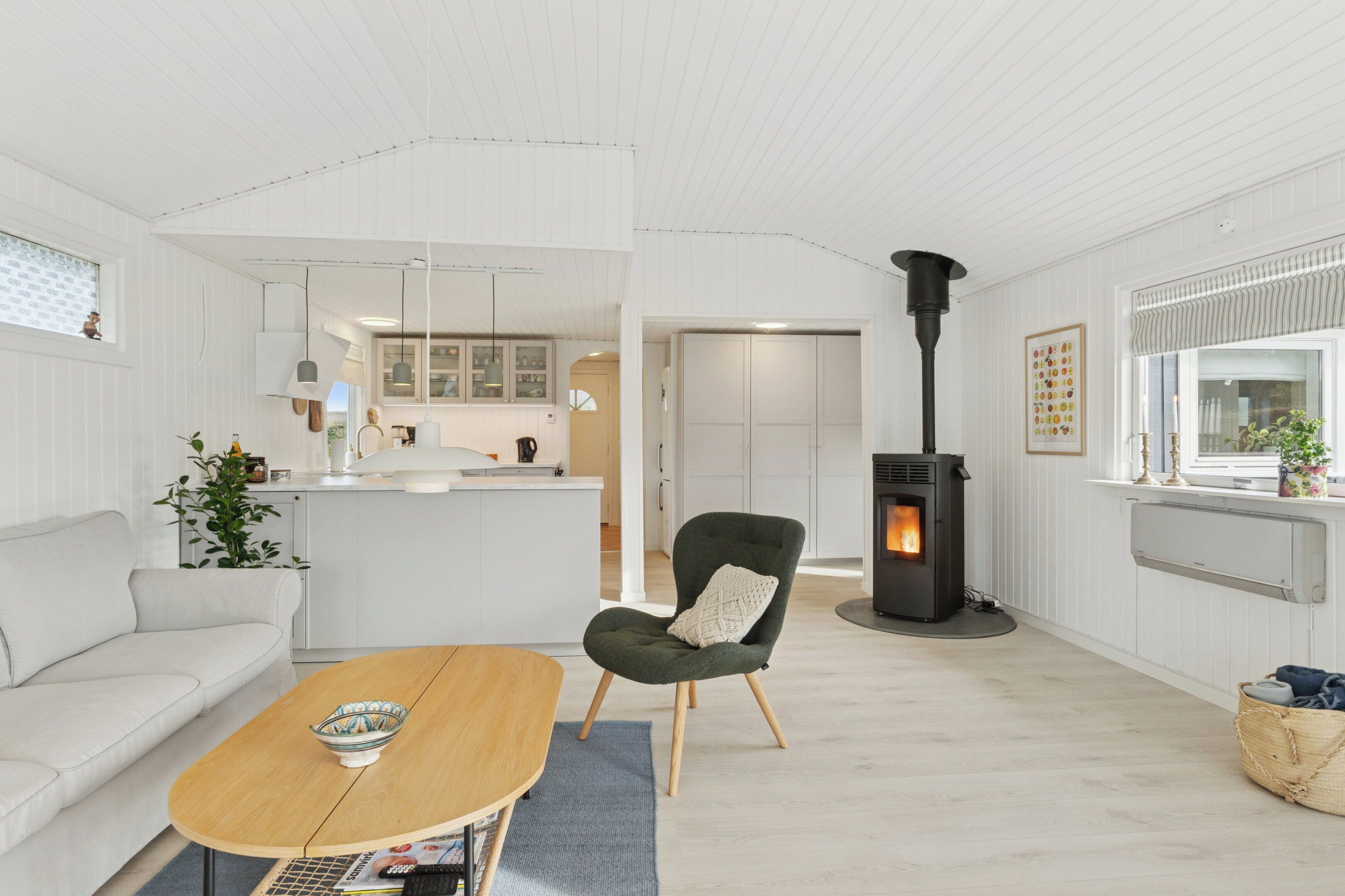 Una sala de estar moderna con un sofá, una mesa de centro de madera, un sillón verde, una chimenea y una cocina al fondo.