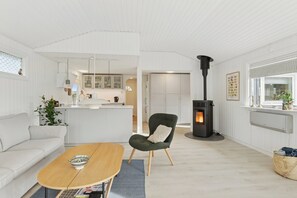 A modern living room with a sofa, a wooden coffee table, a green armchair, a fireplace, and a kitchen in the background.