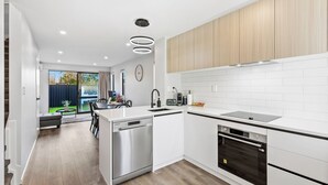 A modern kitchen with white cabinetry, stainless steel appliances, and a wooden floor. - 4BR Townhouse for Families Zodiak Stays (Auckland)
